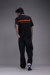 Person wearing a boxy fit black t-shirt with an orange Mclaren formula 1 team logo showing backside of the shirt