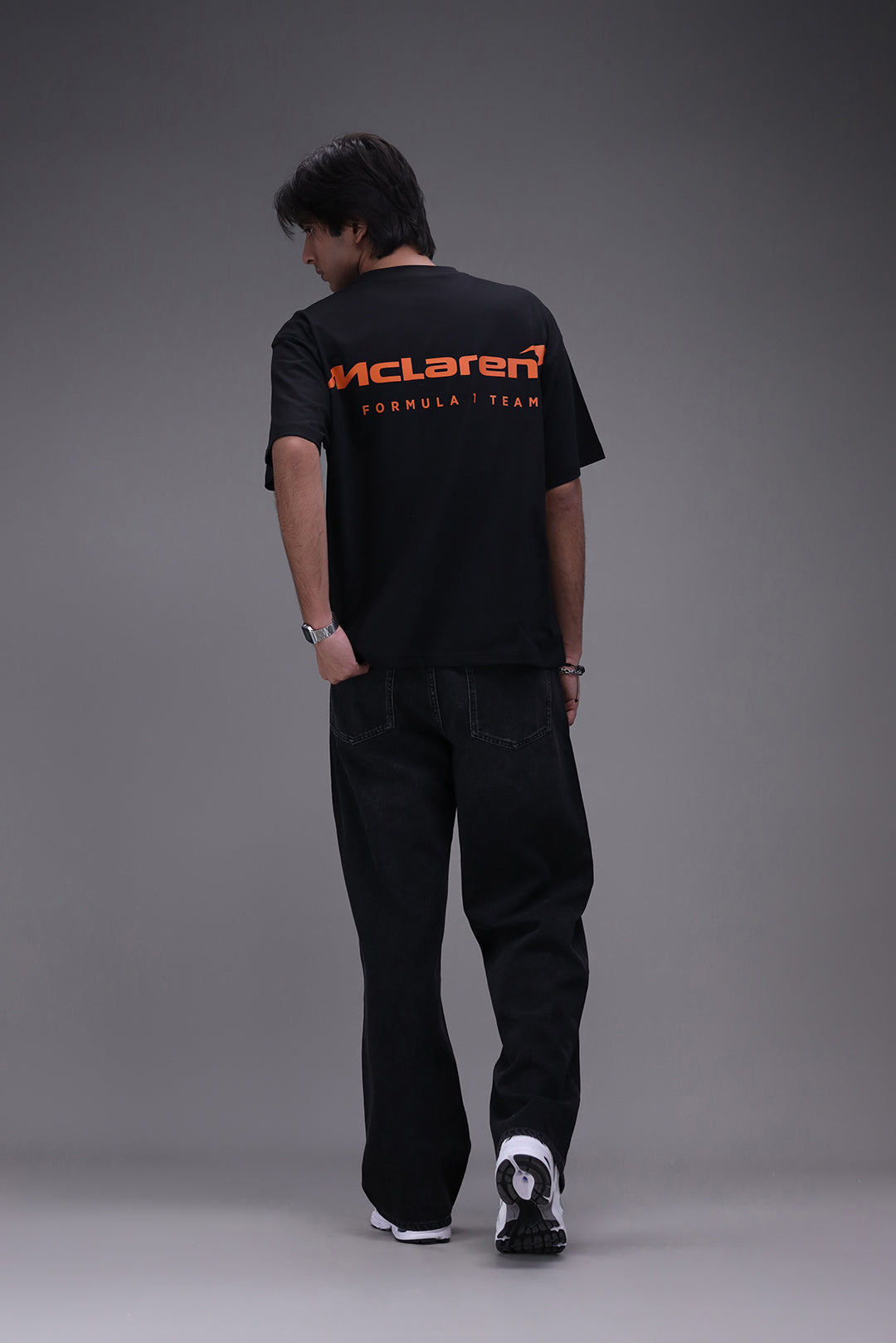 Person  wearing a boxy fit black t-shirt with an orange Mclaren formula 1 team logo showing backside of the shirt